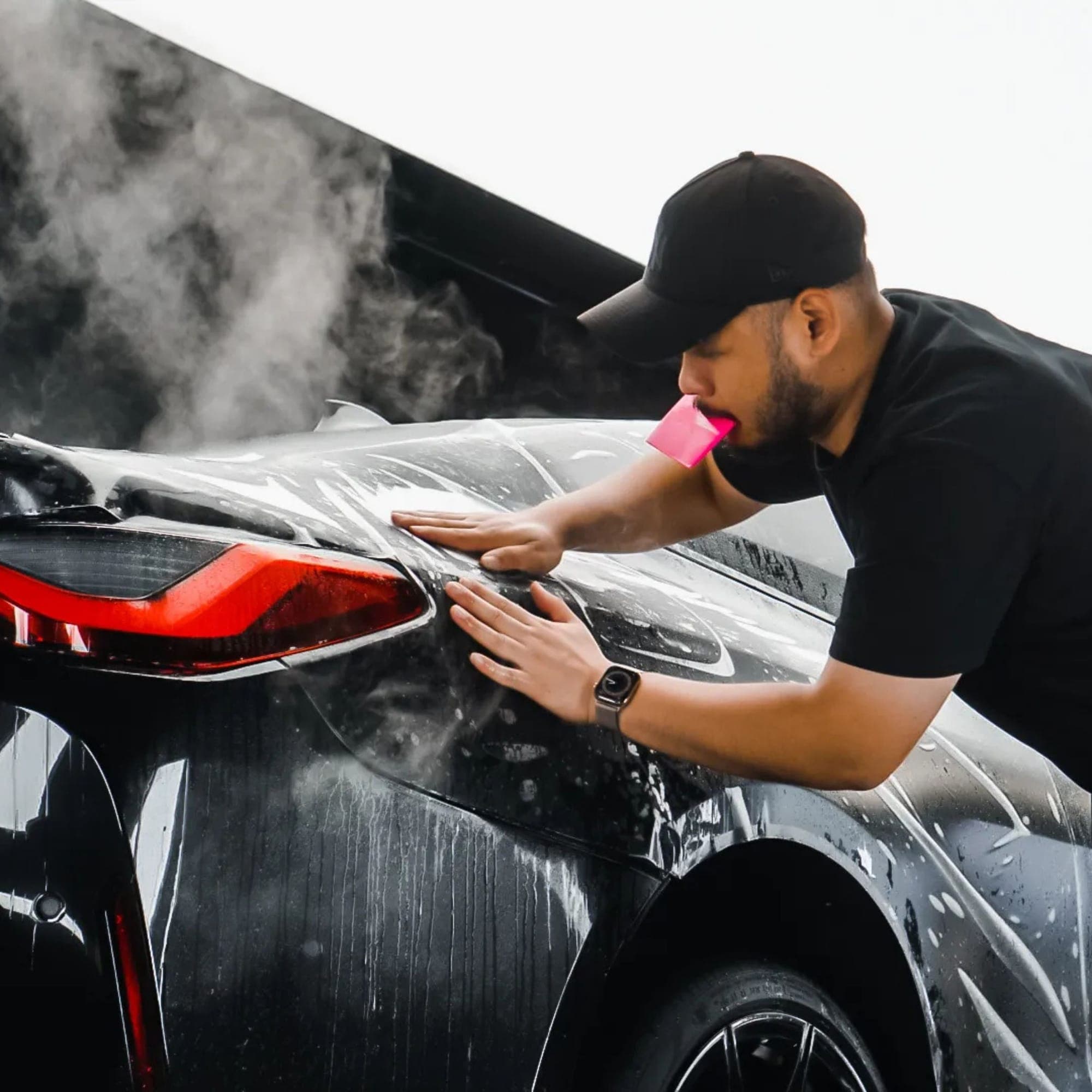 A technician smoothing film by hand onto a car’s rear quarter