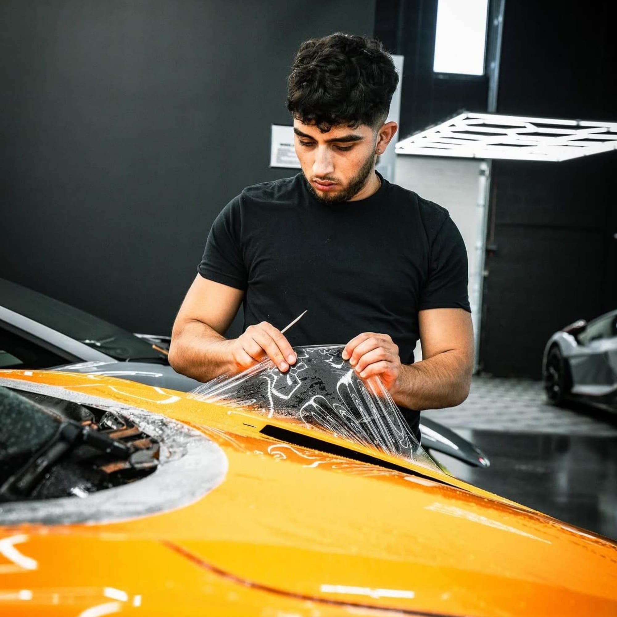 A technician lifting protective film on a yellow car bonnet