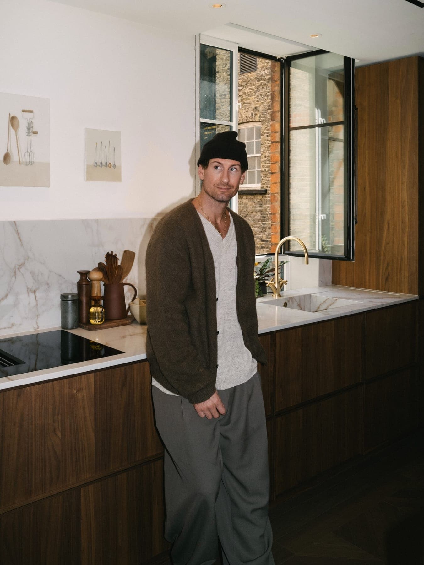 Person in a beanie and cardigan standing in a kitchen