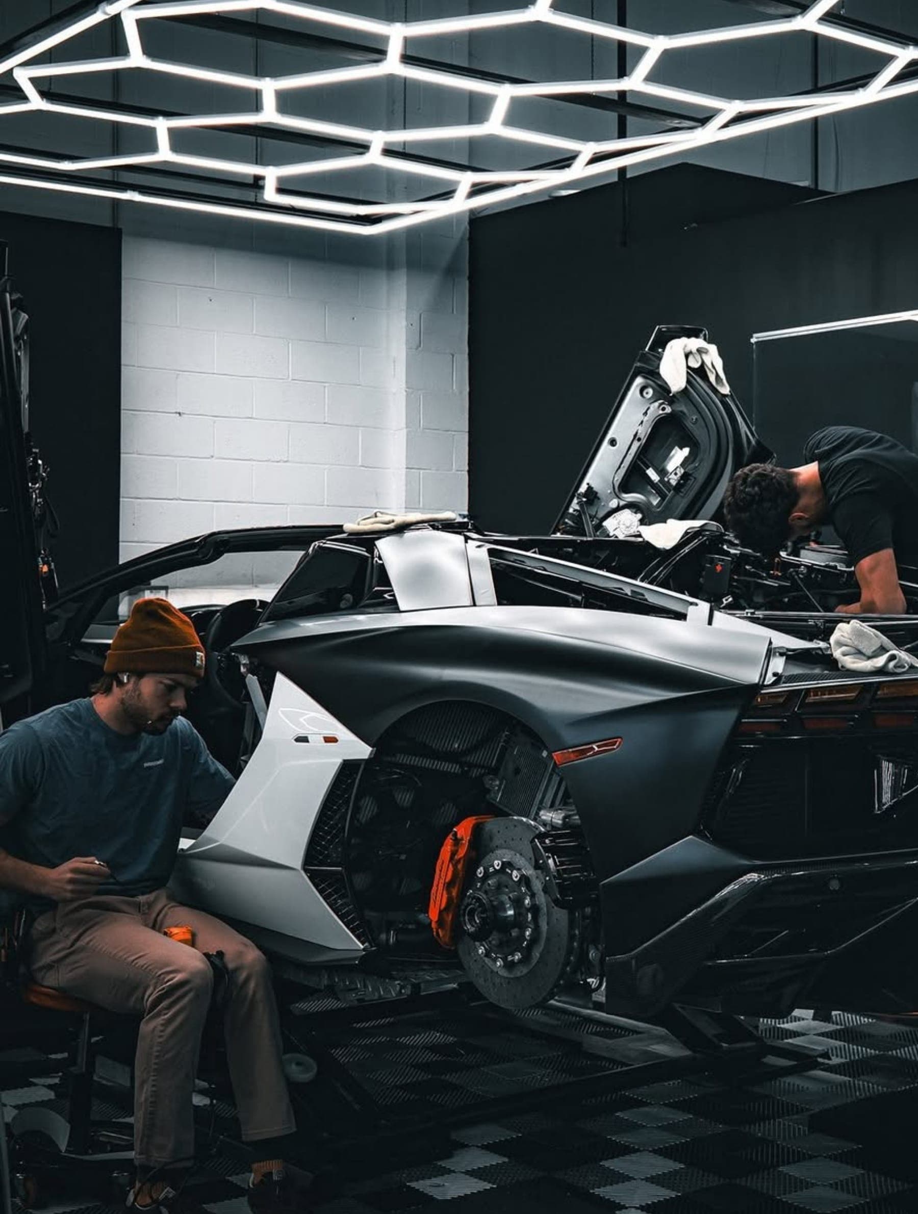 Technicians working on a car in a studio lit by hexagonal ceiling lights